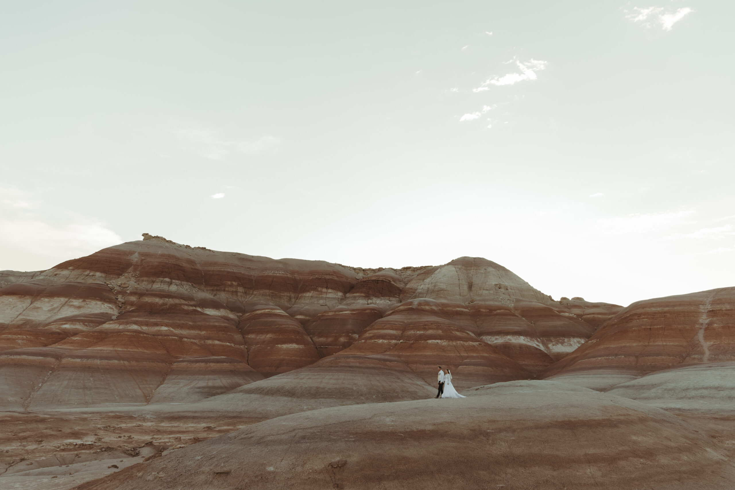Bride and groom standing on hill in the distance surrounded by Southern Utah red rocks.